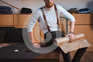 cropped shot of young male fashion designer sitting on table with fabric and sewing tools