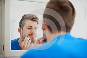 Should I zap this zit or not. Cropped shot of a young man squeezing a pimple in front of a bathroom mirror.