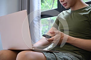 Young man using smart phone and laptop in living room.