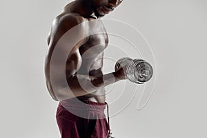 Cropped shot of young muscular african american man lifting weights, standing isolated over grey background. Sports
