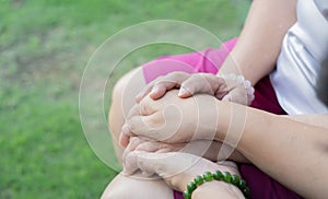 Cropped shot of young woman hands holding old woman hands over green grass background