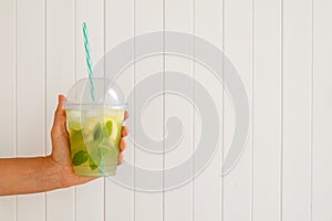 Cropped shot of young woman holding a glass of iced lemonade. Female with refreshing non alcoholic mojito drink with lemon slices