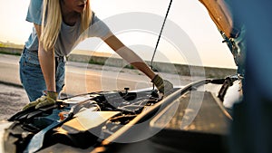 Cropped shot of young woman looking under the hood of her broken car, trying to repair it on her own while waiting for