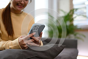 Cropped shot of young woman sitting on couch at home and typing message on mobile phone