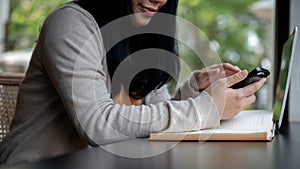 A cropped side view image of an Asian woman using her smartphone while sitting in a coffee shop