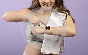 Cropped smiling young european plus size lady in sportswear checks pulse on fitness tracker