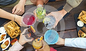 Cropped top view of an unrecognizable group of people in a bar restaurant making a celebratory toast holding colorful cocktails.