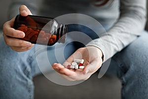 Cropped upset european young lady suffering from depression, grief and loneliness puts a lot of pills in her hand