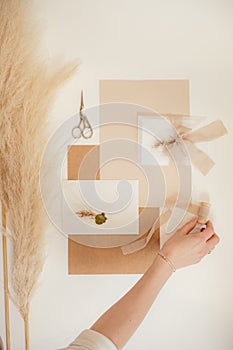 Cropped vertical photo woman hand, peach composition paper envelopes, ribbons, scissors, wax, cut out handmade jobbing.
