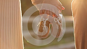 Cropped video of couple, man and pregnant wife are holding hands and warm baby shoes on nature autumn background