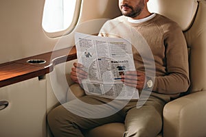 cropped view of bearded man holding newspaper in private jet.