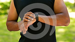 Cropped view of black guy checking his smartwatch or fitness tracker while working out outdoors