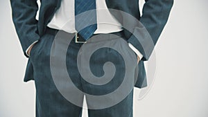 Cropped view of businessman in dark suit and blue tie putting his hands in pockets over white background.