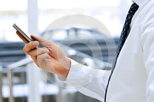 Cropped view of Businessman holding the mobile phone standing in front the window