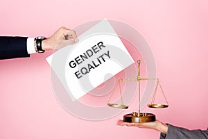 Cropped view of businessman holding placard with gender equality lettering near businesswoman with golden scales on pink