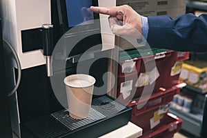 A man buys coffee from a coffee machine. cropped view of businessman pushing button on coffeemaker while preparing