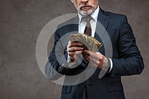 View of businessman in suit holding dollar banknotes in hands on grey