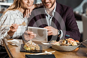 Cropped view of couple using digital device while eating sushi