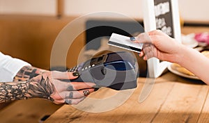 Cropped view of customer holding credit card near payment terminal in cafe.