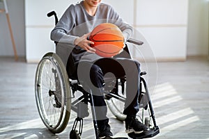 Cropped view of disabled teenager in wheelchair holding basketball at home. Impairment and sports concept