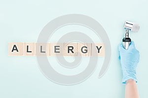 Cropped view of doctor holding dermatoscope near wooden blocks with allergy inscription isolated on blue.