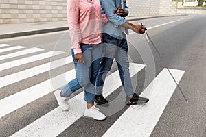 Cropped view of female caregiver assisting visually impaired black man with cane cross city street, closeup