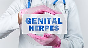 Cropped view of female doctor in a white coat and pink sterile gloves holding a card with words - GENITAL HERPES