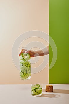 Cropped view of female hand holding bottle filled with water and sliced cucumbers