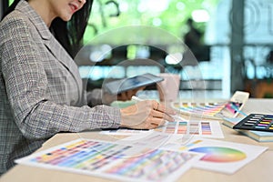 Cropped view of female interior designer using digital tablet and working with color swatches at workplace