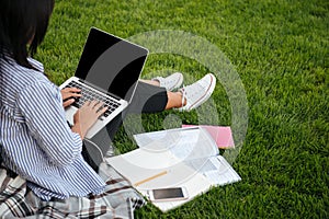 Cropped view of female student typing on laptop, sitting on grass, outdoor