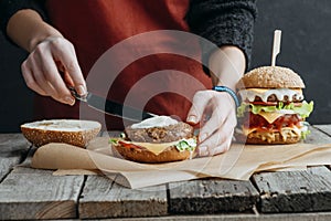 cropped view of girl in apron making tasty homemade cheeseburgers on baking paper