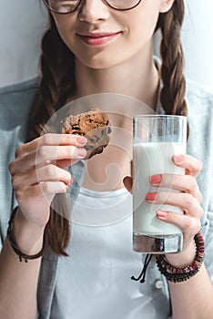 cropped view of girl with cookie and milk