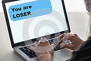 Cropped view of girl typing on laptop keyboard with you are loser message on screen, cyberbullying concept.