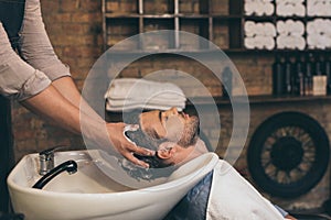 Cropped view hairstylist washing clients hair in barber