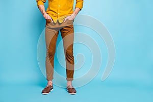 Cropped view of his he young guy wearing brown pants orange formal casual shirt holding hands in pockets  on
