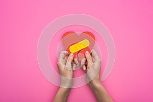 Cropped view of holding broken paper heart with patch isolated on pink background