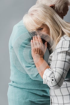 cropped view of husband hugging retired wife covering face while crying isolated on grey.