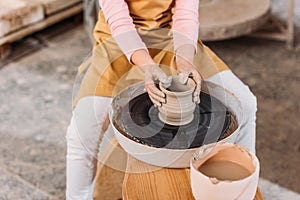 cropped view of kid making ceramic pot on pottery wheel