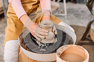 cropped view of kid making ceramic pot on pottery wheel