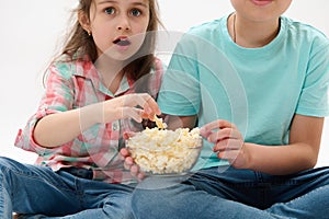 Cropped view kids with a bowl of popcorn, looking fascinated while watching movie, isolated on white studio background