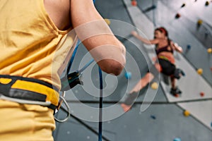 Cropped view of male instructor holding rope, while woman in safety equipment and harness training on the artificial