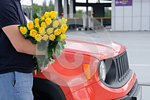 Cropped view of a man with a bouquet of yellow roses and a car in the parking lot. Travel concept