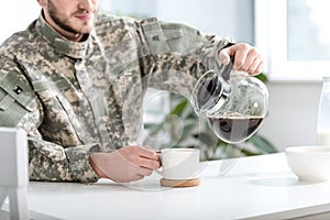 Orezaný človeka v maskovanie jednotný odlievanie káva v pohár 