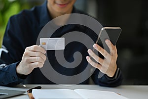 Cropped view of man holding credit card and making payment on internet via smart phone. Online shopping, e-commerce