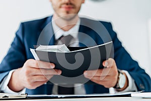 View of man holding envelope with dollar banknotes near laptop on table