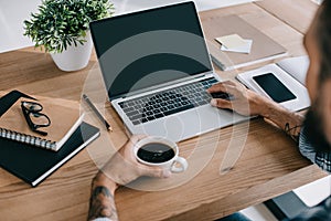 cropped view of man using laptop and holding cup of coffee