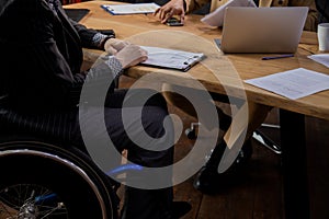 Cropped view of a man in a wheelchair sitting at a table. Two men in formal suits are having a business conversation.