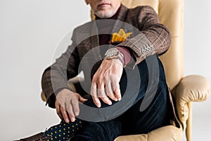 Cropped view of mature man sitting in armchair with crossed legs isolated