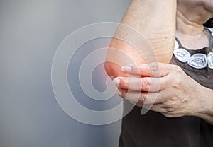 Cropped view of old Asian woman's hand holding elbow with elbow pain. Arthralgia, arm pain photo
