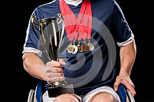 Cropped view of paralympic in wheelchair with champion goblet and gold medals